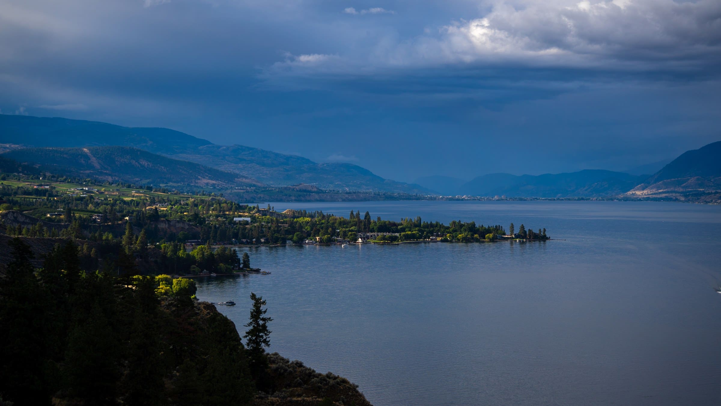 The Naramata peninsula reaching into Okanagan Lake under a dramatic, cloudy sky.